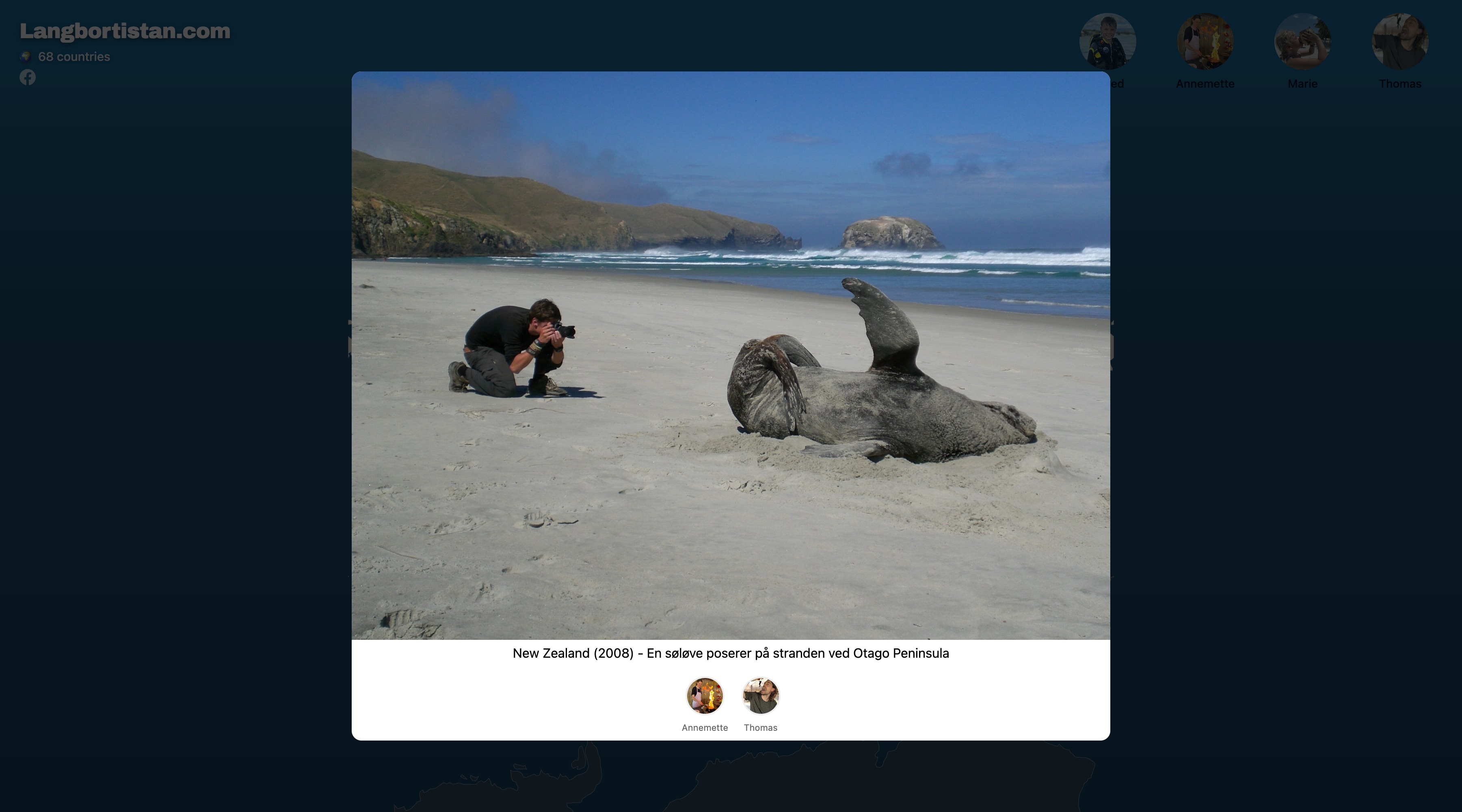 A trip detail open over the map: a photograph of a sea lion lying on a wide sandy beach while a man kneels to photograph it, captioned 'New Zealand (2008) - En søløve poserer på stranden ved Otago Peninsula', with the avatars of Annemette and Thomas below it
